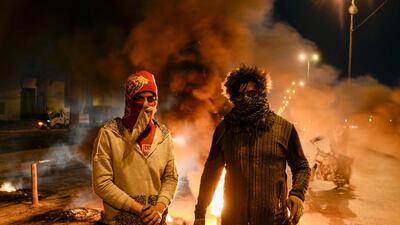 Masked anti-government protester stand before flaming tyres at a make-shift roadblock in the central Iraqi holy shrine city of Najaf. AFP