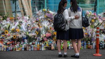 A girl comforts her friend as they pause next to flowers and tributes laid at the scene of a knife attack on a group of schoolchildren in Kawasaki, Japan. Getty Images