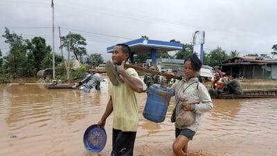 Victims wade through a flooded street as they carry drinking water in Sanamxai, Attapeu province. AFP