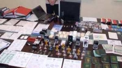 One of the two suspects in handcuffs stands with fake credit cards, chequebooks, passports and visas that were seized by police.