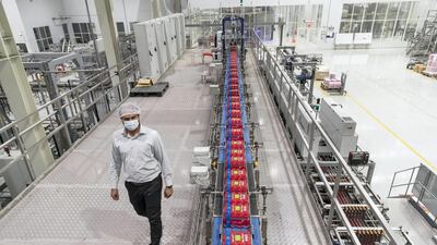 A masked supervisor walks past sealed packets of Mai Dubai bottles that are in line to be loaded and dispatched. Antonie Robertson/The National