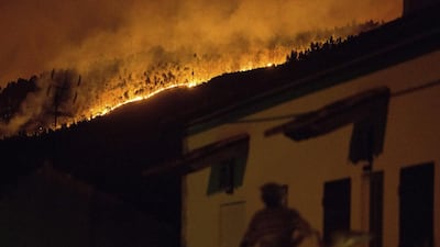 A man on the balcony of a house looks up at a forest fire raging on a hillside above the village of Avelar, central Portugal. Armando Franca / AP Photo