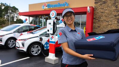 A Domino's delivery driver next to the company's new vehicles.