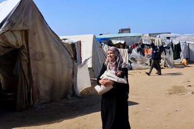A displaced Palestinian woman, who fled her house due to Israeli strikes, carries a child as she walks through a camp Rafah.