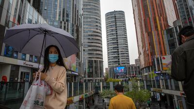 A woman wearing a face mask to help protect against COVID-19 walks through an office and shopping complex on a rainy day in Beijing. A Chinese border city hit by a fresh outbreak of COVID-19 this week began a five-day drive Friday to vaccinate its entire population of 300,000 people. AP Photo