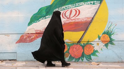 A woman in Tehran walks past a mural featuring the Iranian flag. Photo: West Asia News Agency via Reuters