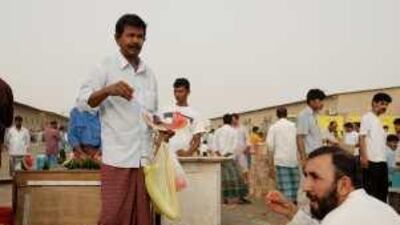 Workers, and taxi drivers sell and buy fruit and vegetables in a make shift market between labour camps in Mussafah East.