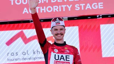 UAE Team Emirates rider Jay Vine celebrates on the podium in his leader's red jersey.