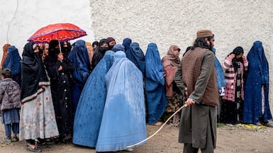 A Taliban member stands guard as Afghan women wait to receive food supplies in Kabul. AFP