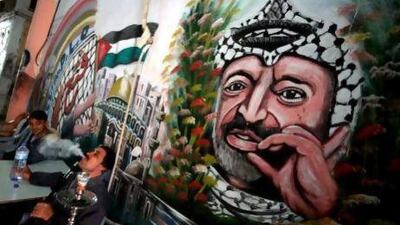 Palestinian men sit in a cafe near a mural of their late leader Yasser Arafat in the West Bank city of Jenin. Arafat’s wife Suha alleges he was poisoned before his 2004 death.