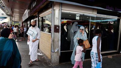 Chehrazad (2nd R), 36, talks on a mobile phone, while a man fundraises for a mosque (L) in Mantes-la-Jolie.