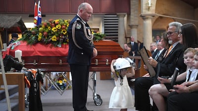 Rural Fire Service Commissioner Shane Fitzsimmons looks at Charlotte O'Dwyer, daughter of New South Wales Rural Fire Service volunteer Andrew O'Dwyer, wearing her father's helmet during a funeral at Our Lady of Victories Catholic Church in Horsley Park, Sydney. EPA