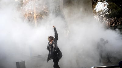 In this photo, a university student attends a protest inside University of Tehran while a smoke grenade is thrown by anti-riot police on December 30. AP