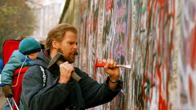 A sight-seeing West Berliner carries his baby and uses a hammer and chisel to carve out a piece of the Berlin Wall. Many souvenir hunters come to the Berlin to break pieces off the crumbling wall. AP Photo