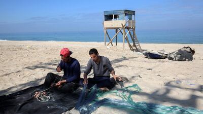 Palestinian fishermen mend a fishing-net as they sit along the sandy beach at Khan Yunis in the southern Gaza Strip. AFP