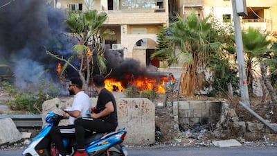Men drive past a vehicle following clashes in the Khalde area, south of Beirut.
