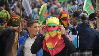 A young man uses a PKK flag to conceal his face - and the flag of the Syrian-Kurdish YPG militia as a bandana to cover his head - as he marches at Nowruz celebrations in Diyarbakir on March 21, 2016. Josh Wood for The National