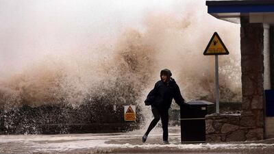 A woman stands in front of a huge wave on the seafront, in Rhyl, Wales, on Thursday. Gale-force winds hit Scotland, causing a fatal truck accident, halting all trains and leaving tens of thousands of homes without electricity as much of northwestern Europe braced for a storm that was expected to bring flooding to coastal areas. Peter Byrne / AP Photo