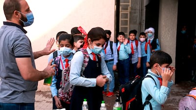 A teacher sanitises pupils' hands in the playground at a school in Baghdad, one of the many anti-coronavirus measures. AP