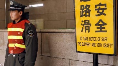 A security guard stands next to a sign which reads in English, "To Take Notice of Safe The Slippery Are Very Crafty", at the entrance of a Beijing shopping mall.
