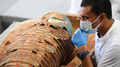 Archaeologists inspect a mummy, wrapped in a burial shroud adorned with brightly coloured hieroglyphics pictorials, during the unveiling of an ancient treasure trove of more than a 100 intact sarcophagi. AFP