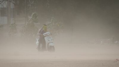 A couple ride a scooter amid dust stirred up by strong wind in Ahmedabad. Reuters