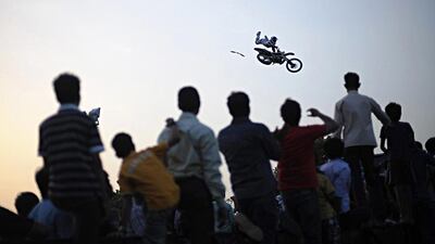 An Indian crowd watches a professional motorcyclist preform a stunt with his motorcycle after coming off a ramp during a motorcycle show near India Gate in New Delhi on June 30, 2012. The stunt was part of the Red Bull X- Fighters Jams, a series of exhibitions that travels around the world. AFP PHOTO/ Roberto Schmidt