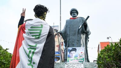 A young person draped in an Iraqi national flag flashes the victory gesture while standing before a statue of 19th century Iraqi cleric and poet Mohamed Said Al Habboubi at the square named after him in Iraq's southern city of Nasiriyah in Dhi Qar province. AFP
