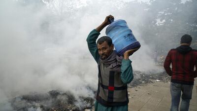 A Bangladeshi man carries a water container while walking past burning rubbish in Dhaka. Abir Abdullah / EPA