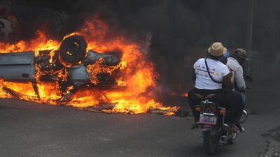People on a motorcycle ride near a burning car. Reuters