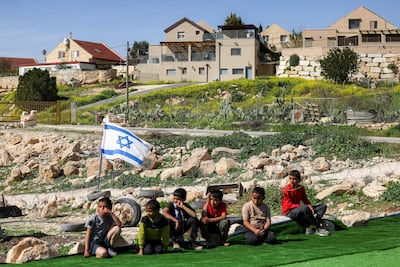 Palestinian boys sit on a football pitch at Umm Al Kheir, east of Yatta in the south of the occupied West Bank, surrounded by Israeli flags, placed by settlers after the pitch was marked for demolition by Israeli authorities on February 12, 2026. AFP
