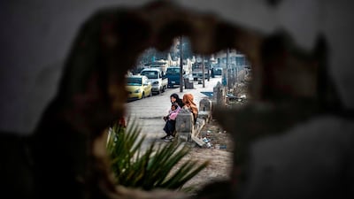 Women sitting by a street are seen through a bullet hole in the northern Syrian city of Raqa, the former Syrian capital of ISIS. AFP