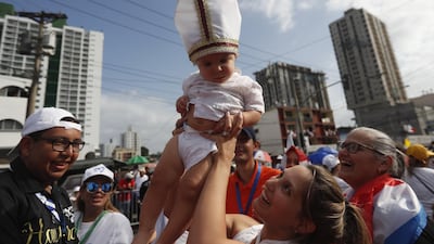A woman holds a baby wearing a miter as they await the arrival of Pope Francis in Panama City. EPA