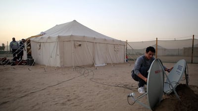 A member of the Al Shimmari family fixes a satellite dish outside one of the camp's tents on January 13, 2017. Yasser Al Zayyat / AFP