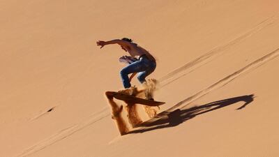 A tourist sandboards down a dune in the Dubai desert