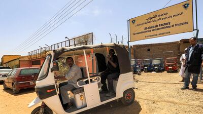 Workers test-drive a new electric tuk-tuk in the factory grounds.