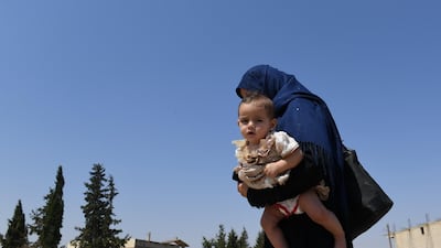 A Syrian woman holds her child as she walks across the Abu Duhur crossing. AFP