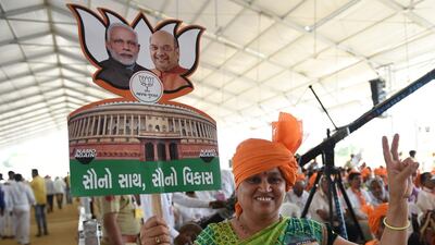An Indian supporter of the Bhartiya Janta Party (BJP) carries a cut-out of the Indian Parliament with the images of Prime Minister Narendra Modi and BJP President Amit Shah during a rally in Amreli, some 250km from Ahmedabad, on April 18, 2019. More than 157 million of the 900 million electorate are eligible to cast ballots on the second of seven days of voting in the world's biggest election. / AFP / SAM PANTHAKY