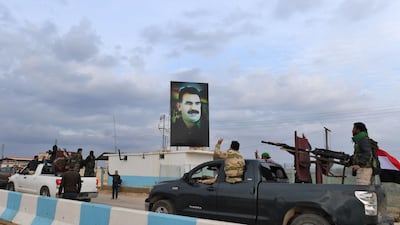 A convoy of pro-Syrian government fighters flashing the victory gesture as they ride through the windows of pickup trucks upon arriving in Syria's northern region of Afrin, with a portrait of the Kurdistan Worker's Party (PKK) leader Abdullah Ocalan seen on a banner in the background. George Ourfalian / AFP