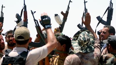 Iraqi government forces and members of the Popular Mobilisation units raise their weapons on the front line during battles with ISIS on the road leading to Saqlawiya, in Iraq's Anbar province, on August 4, 2015.