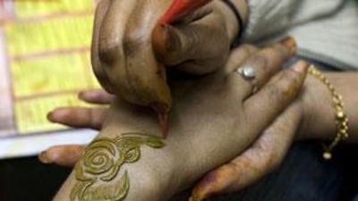 A salon manager applies red henna, which is less likely to contain large proportions of the chemical PPD, to a customer.