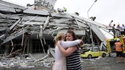 Two women hug each other in front of a collapsed building in central Christchurch yesterday. A strong quake hit New Zealand's second-biggest city , trapping people beneath rubble and sparking fires.