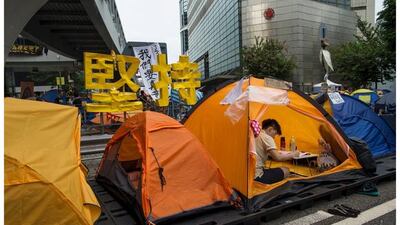 Top, a student does his homework in a tent with a sign that reads, "persist on" in the background in the financial Central district in Hong Kong on October 25, 2014, and bottom, the same sign on September 23, 2015. Reuters