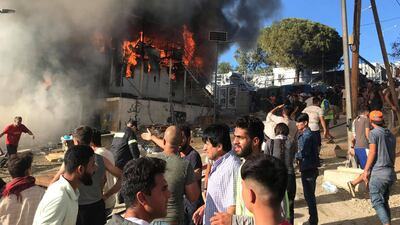 Migrants stand next to a burning container during a fire in Moria camp on the island of Lesbos, Greece, September 29, 2019. Ihab Abassi/Handout via REUTERS