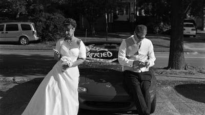 Newlyweds sit on the hood of a Mazda coupe. The bride has a bouquet in one hand, the groom is smoking a cigarette. They are seemingly looking at their phones. When the viewer notices their absence, the disconnected nature of the scene strikes. Courtesy: Eric Pickersgill