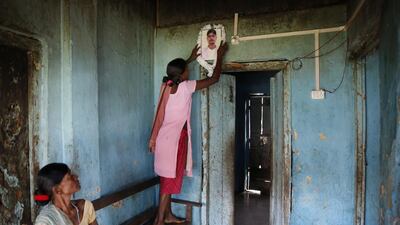 Asrita Tirki puts a garland onto a photo of her husband, who died within a month for not been able to afford treatment in a hospital for his illness, as her mother in law Biro Tirki looks on.