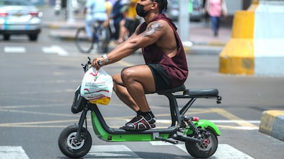 A rider on a seated e-scooter crosses Abu Dhabi's Hamdan Street in 2021. Riders are required by law to wear a helmet, and since this photo was taken, seated scooters have been banned. Victor Besa / The National
