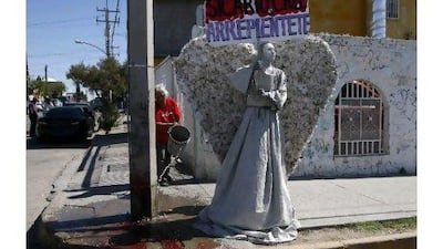 A young member of the Christian church Psalm 100 dressed as an angel holds a sign reading "Hitmen, believe and repent" while a woman throws a bucket of water on a puddle of blood at a crime scene on Saturday where a man was shot dead in Ciudad Juarez. Jose Luis Gonzalez / Reuters