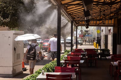 A resident blocks out the sun while walking through misters during a heatwave in Phoenix, Arizona, in July. Bloomberg