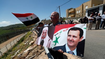 A demonstrator holds portraits of Syrian President Bashar Al Assad next to the ceasefire line between Israel and Syria. EPA